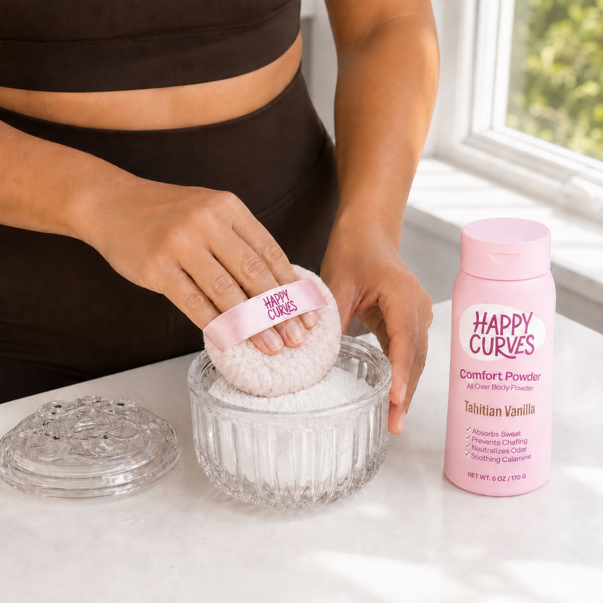 Woman pressing the Happy Curves Comfort Puff into powder in the glass vanity jar beside Tahitian Vanilla Comfort Powder